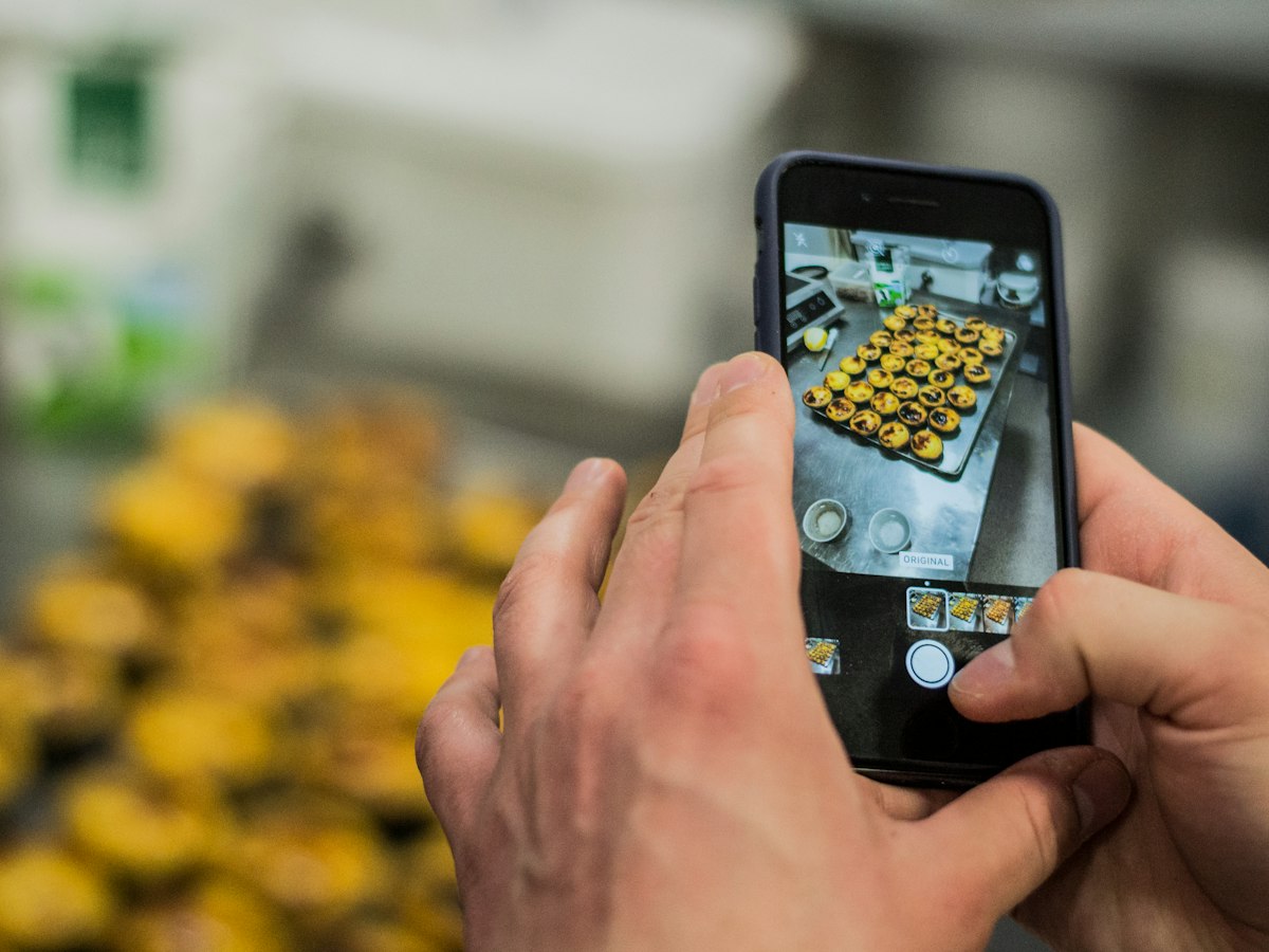 A baker photographing a fresh tray of pastries on a phone in the kitchen